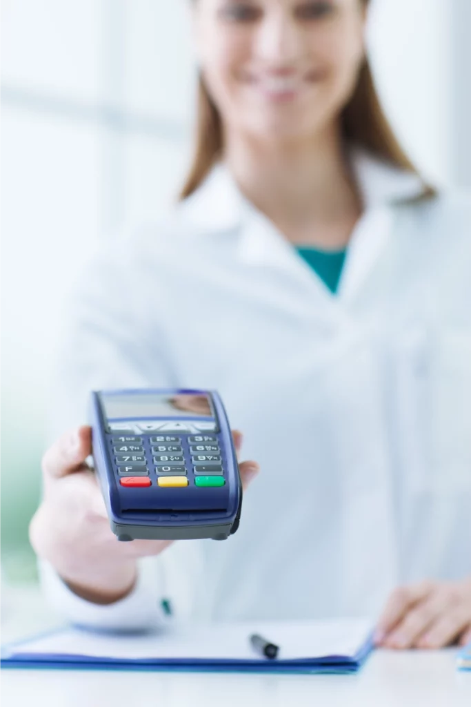 Woman in healthcare setting presenting a credit card processing terminal to a customer for payment
